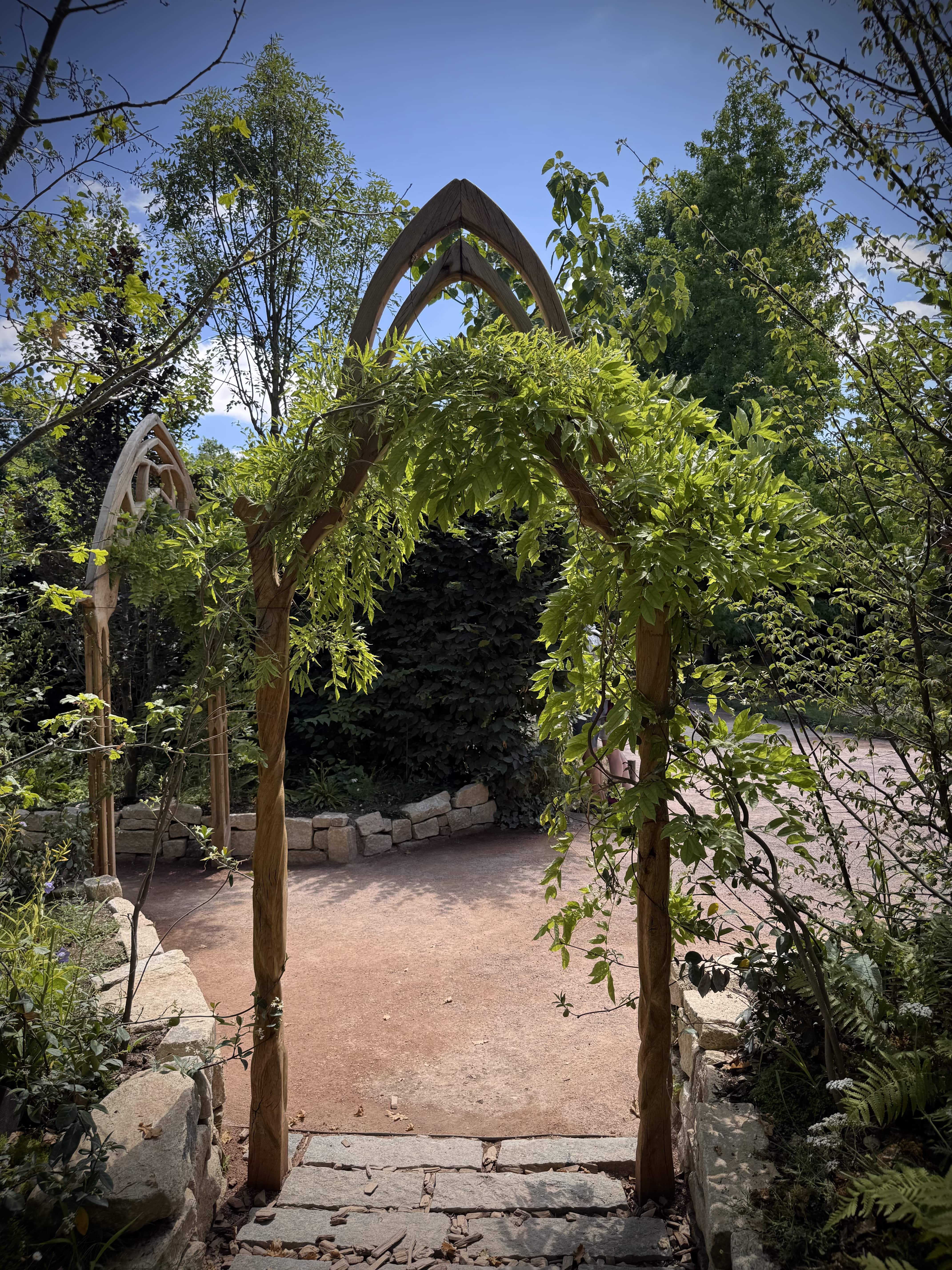 Arche en chêne à l'entrée d'un jardin inspiré des légendes bretonnes, marquant le passage vers un univers fantastique